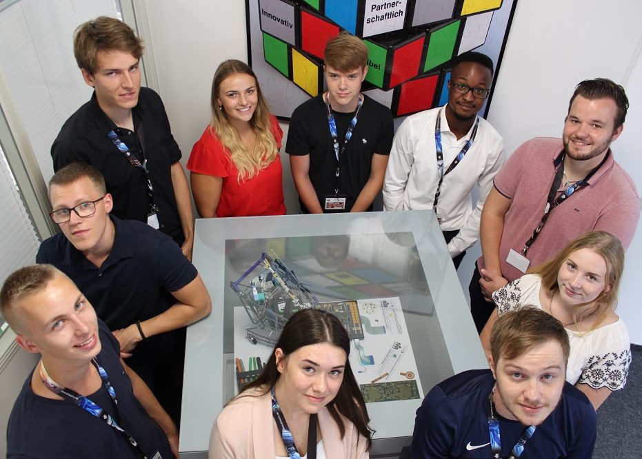 Auszubildende schauen nach oben in die Kamera und stehen um einen straschu Würfel herum.