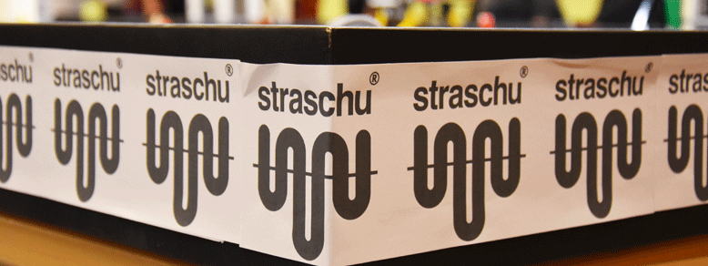 Ein weißes Banner mit dunklem straschu Logo über den Rand eines Tisches geklebt.