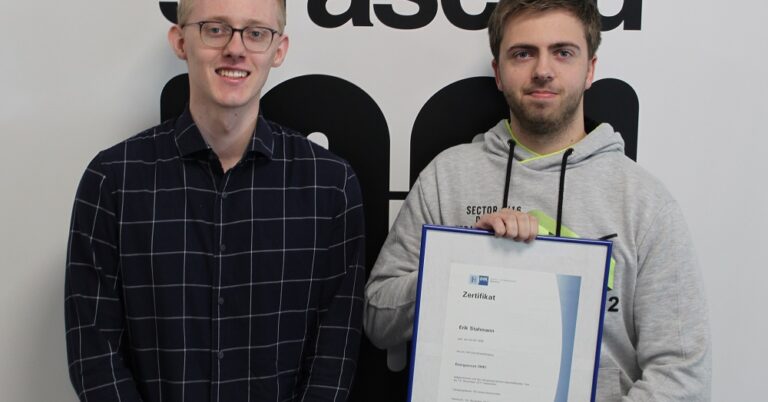 Zwei Männer, die am Projekt Energyscouts mitgewirkt haben, stehen vor einer Wand mit straschu Logo und der rechte hält ein gerahmtes Zertifikat.