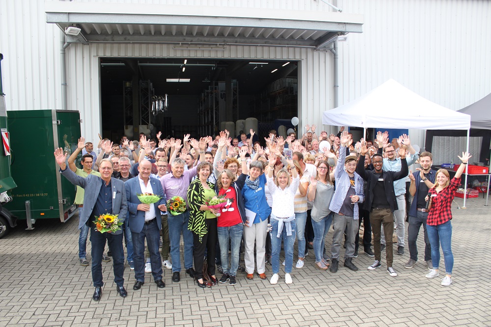 Gruppenbild der straschu Mitarbeiter beim Mitarbeiter-Grillfest, die alle die Arme in die Luft strecken vor einem geöffneten Tor zu einem Lager