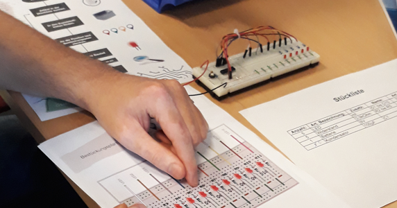 berufsparcours bbs syke Auf einem Tisch liegen Unterlagen und ein Schaltgerät für den Berufsparcours der BBs Syke und eine Person zeigt mit einem Finger auf eine der Unterlagen.