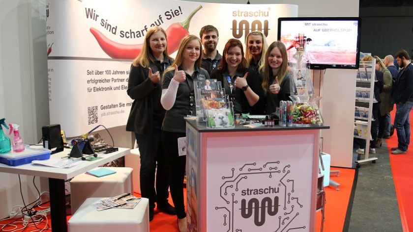 Das Standpersonal auf der Messe steht vor dem Messecounter und macht die Daumen hoch-Geste.