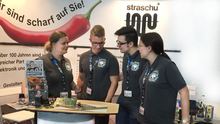 Das straschu Standteam steht vor dem Messecounter auf der vocatium Messe und redet.