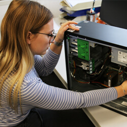 Eine Frau mit langen blonden Haaren, die Auszubildende für IT-Systemintegration ist, arbeitet an einem PC-Gehäuse.
