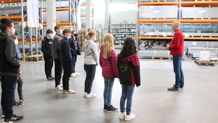 Eine Gruppe von Kindern steht in einer Lagerhalle und schaut zu einem Lagermitarbeiter am Zukunftstag