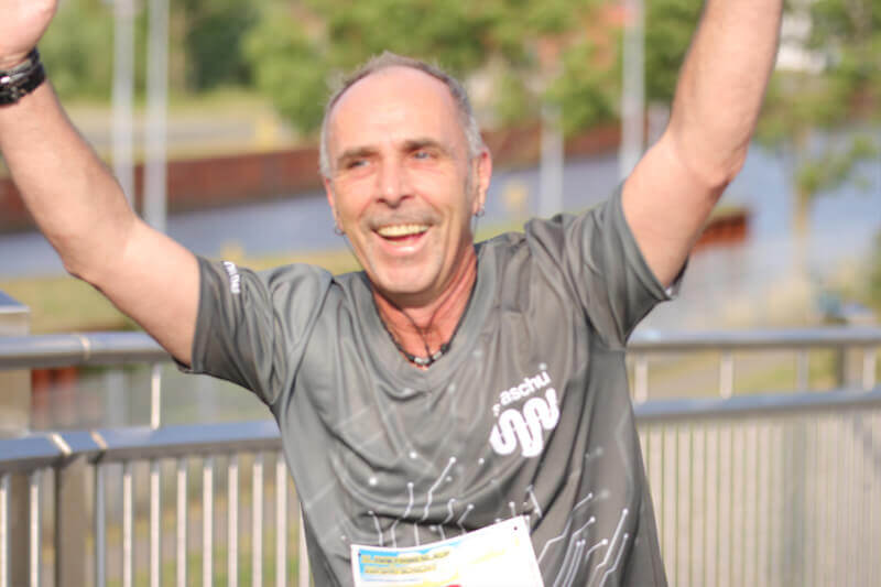 Ein Mann in straschu-Kleidung läuft beim Firmenlauf mit und streckt die Arme in die Höhe.