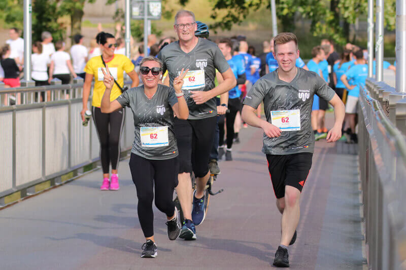Mehrere Mitarbeiter in straschu-Shirts laufen beim Firmenlauf über eine Brücke.