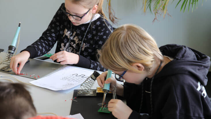 Zwei Kinder sitzen an einem Tisch und löten am Zukunftstag 2024 ihr eigenes Lötprojekt.
