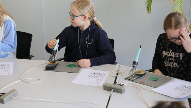Zwei Kinder sitzen an einem Tisch und löten am Zukunftstag 2024 ihr eigenes Lötprojekt.
