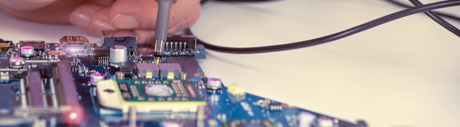 Sliderbild, wie eine Platine händisch geprüft wird.