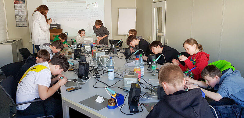 Eine Gruppe von Schülern arbeitet an einem Lötprojekt mit Lötkolben und Leiterplatte am Zukunftstag.