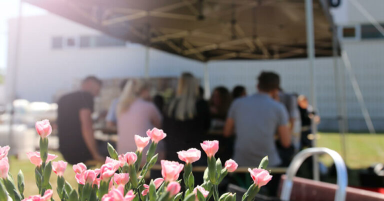Azubi-Grillen 2024 Blumen mit Menschen am Tisch im Hintergrund.