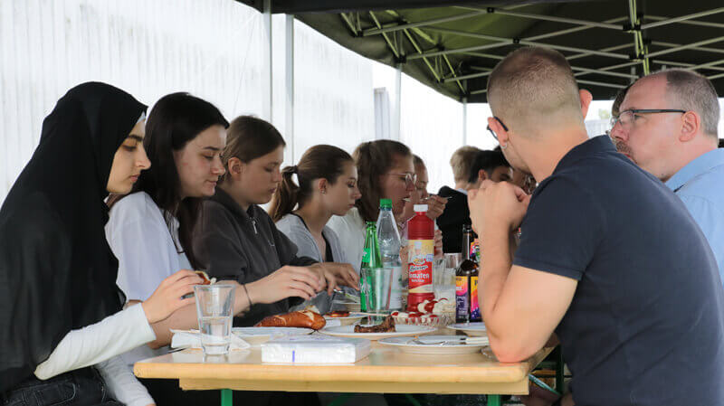 Menschen am einem eingedecktem Tisch unter einem Pavillon.