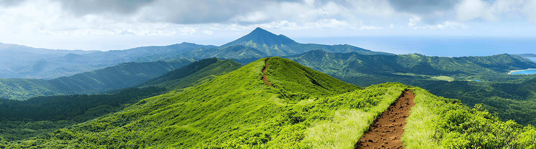 bergige, grüne Landschaft mit Pfad auf dem obersten Hügel und einem See im Hintergrund