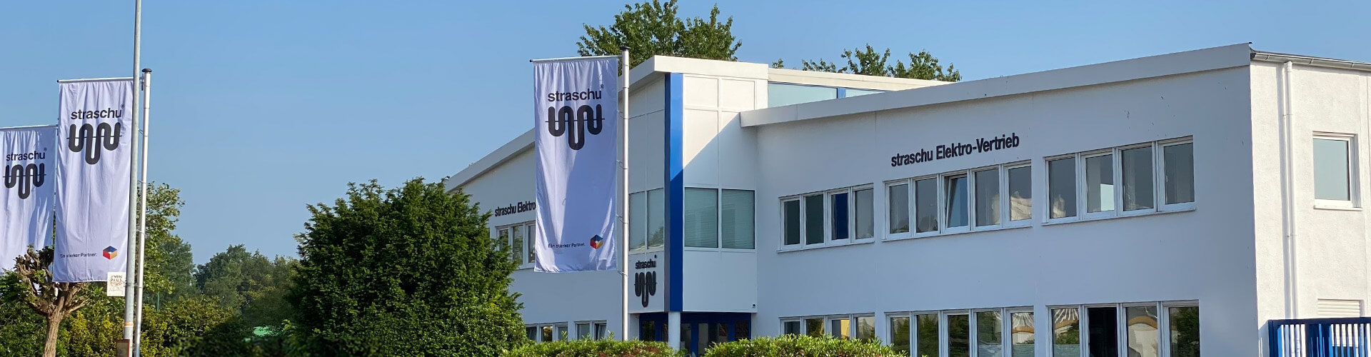 Ein großes weißes Gebäude mit grünen Bäumen und Fahnen davor.