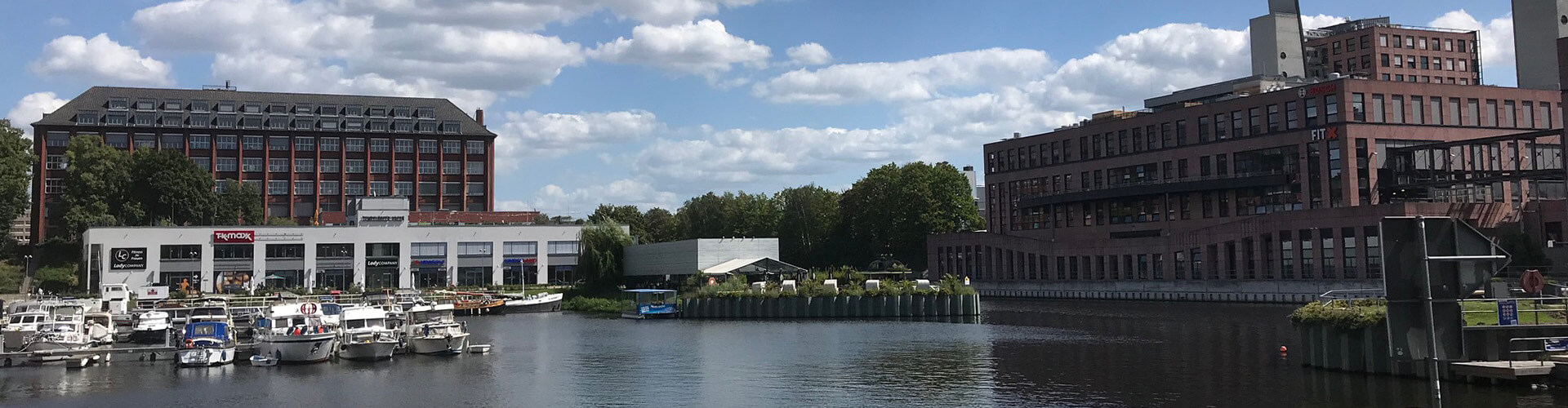 Ansicht auf einen Teich mit einem roten Backsteingebäude rechts und einem Bootsanleger links.