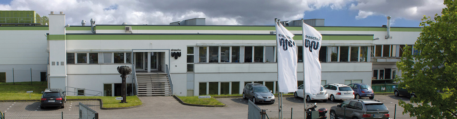 Ansicht auf ein großes Flachdachgebäude mit wehenden Fahen davor.