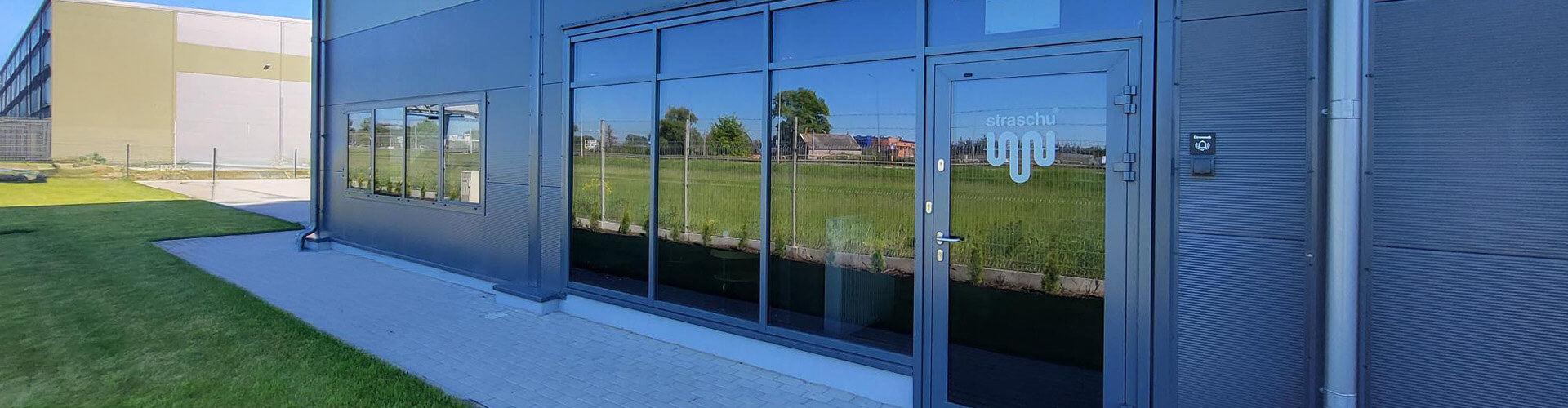 Eine Hauswand mit Glasfront und einer Tür mit straschu Logo.