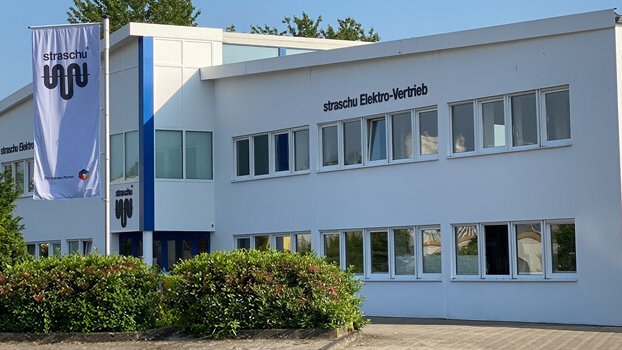 Ein großes weißes Gebäude mit grünen Büschen und einer Fahne davor.