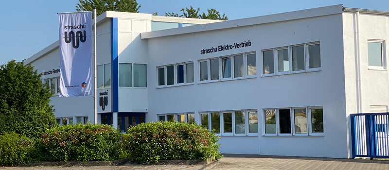 Ein großes weißes Gebäude mit grünen Büschen und einer Fahne davor.