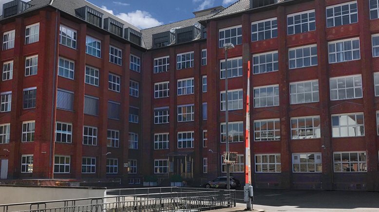 Ein großes rotes Ziegelstein-Gebäude mit vielen Fenstern und einer Schranke vor der Zufahrt.