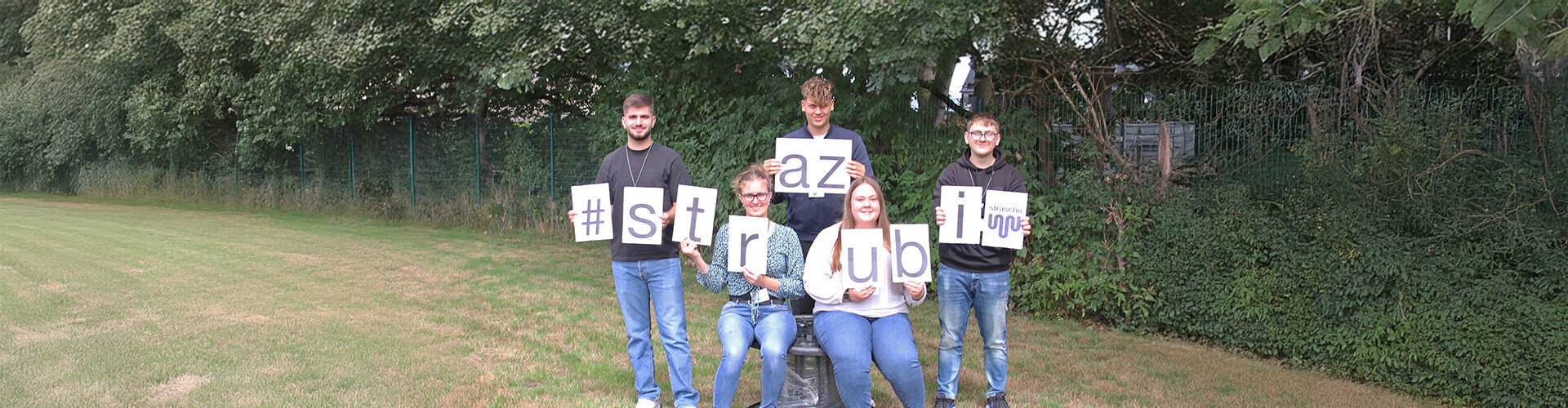 Fünf junge Auszubildende stehen in einer Gruppe und halten die Buchstaben für das Wort "strazubi"