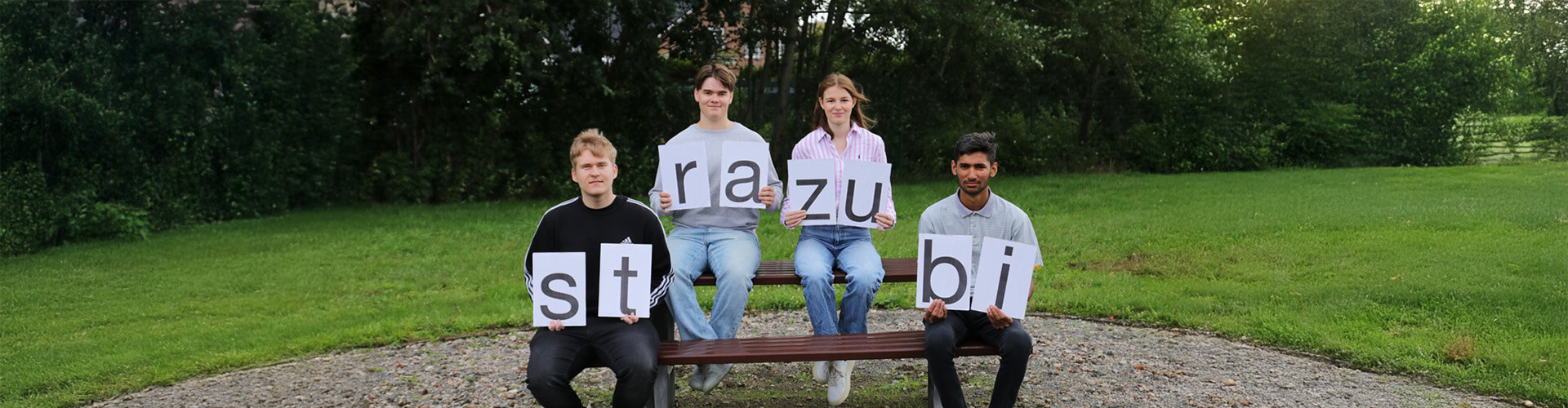 Vier junge Azuis sitzen auf einer Bank und halten die Buchstaben für das Wort "strazubi"