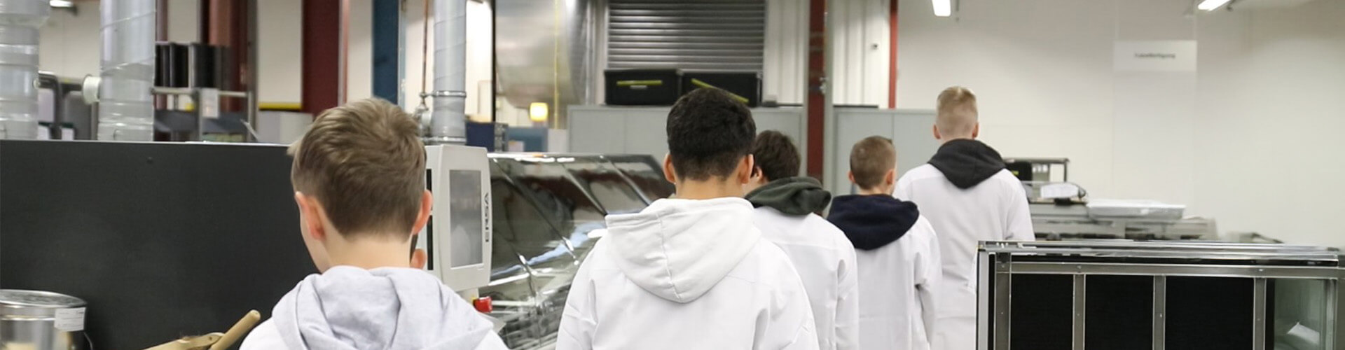 2503 Slider KGS Kirchweyhe Kinder von hinten in weißen Kitteln in einer Fertigungshalle.