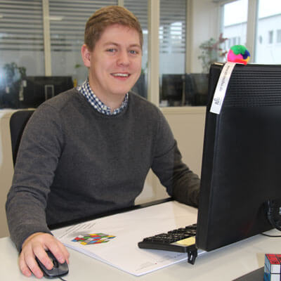 Ein junger Mann, der eine Ausbildung zum Fachinformatiker für Systemintegration macht, arbeitet am Computer und lächelt.