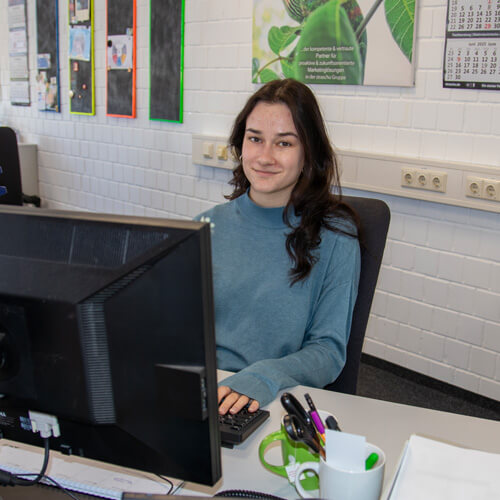 Eine junge dunkelhaarige Frau, die eine Ausbildung zur Personaldienstleistungskauffrau macht, sitzt am Computerarbeitsplatz