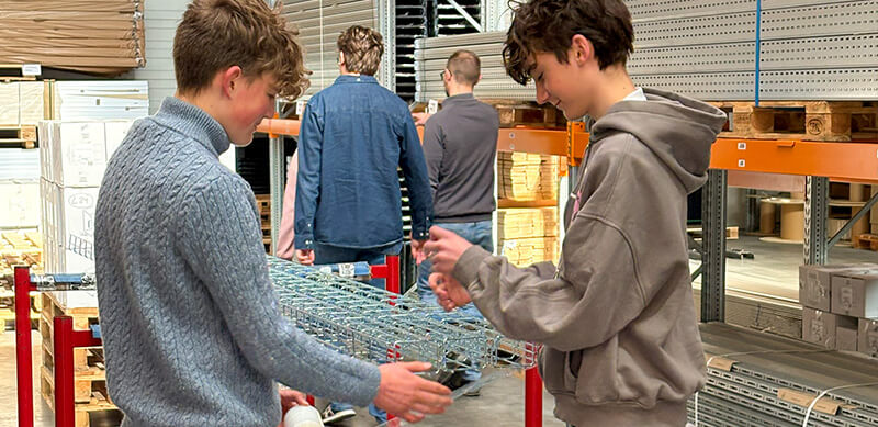 Zwei Jungs packen mit Stretchfolie Gitterrinnen von BAKS im Lager von straschu ein
